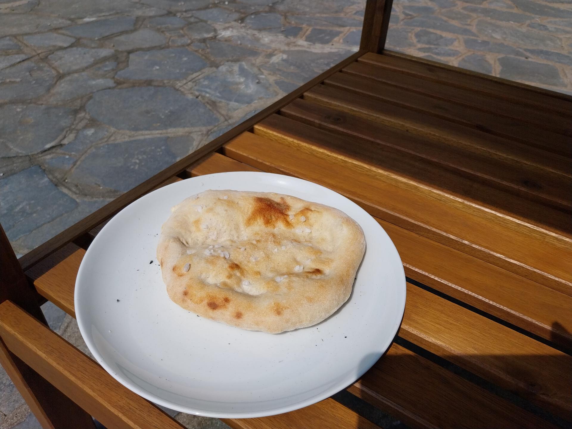 A flatbread on a regular plate: it's only a bit more than half
the plate in diameter, puffed up near the borders and thin in the
middle, and only lightly browned in places, not burnt.
It's sitting on the lower shelf of a wooden table.