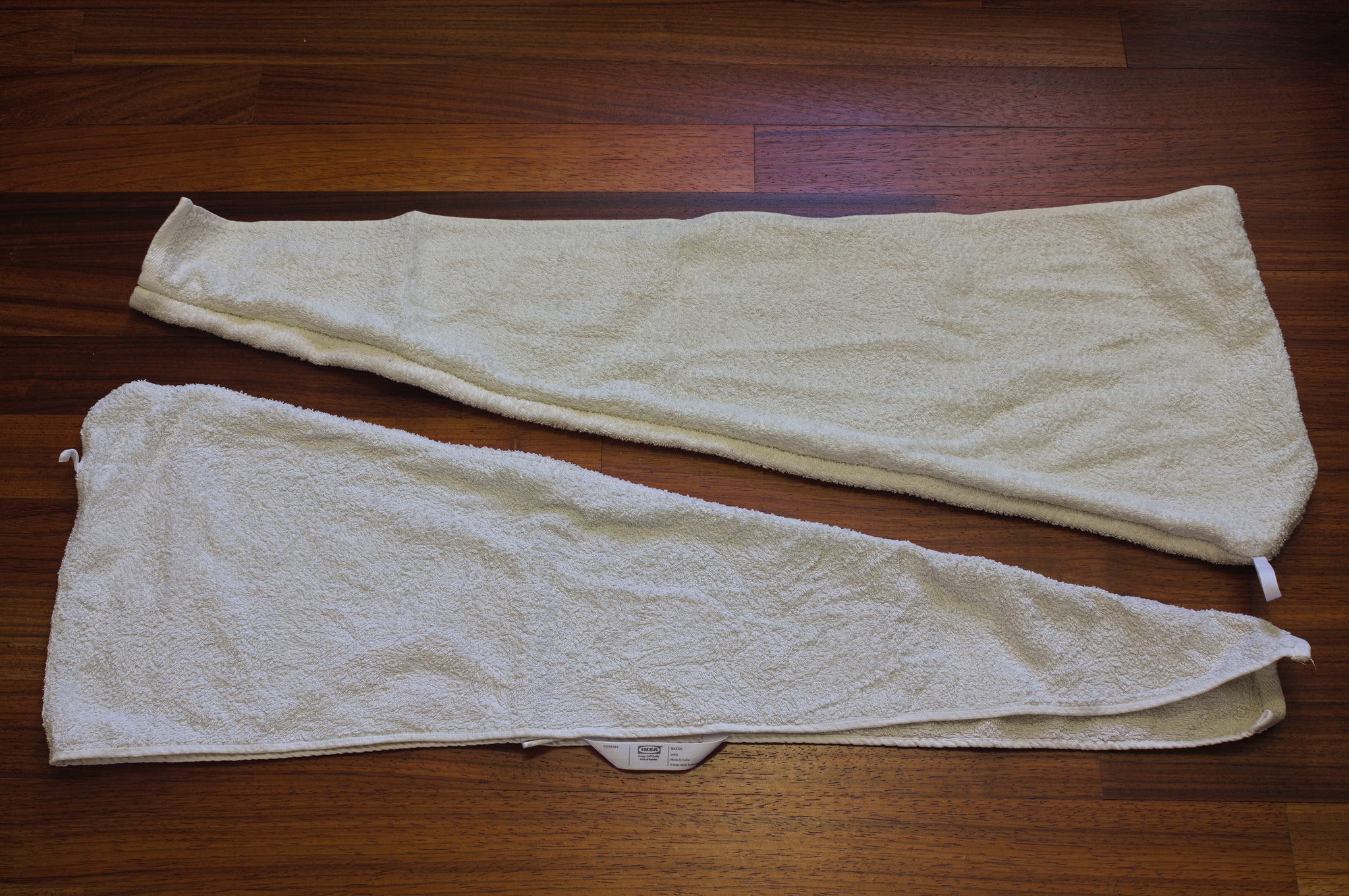 Two trapezoid shaped hoods made out of off-white towels: one is
still looking new, while the other one has been bleached and
roughened by having been washed many times.