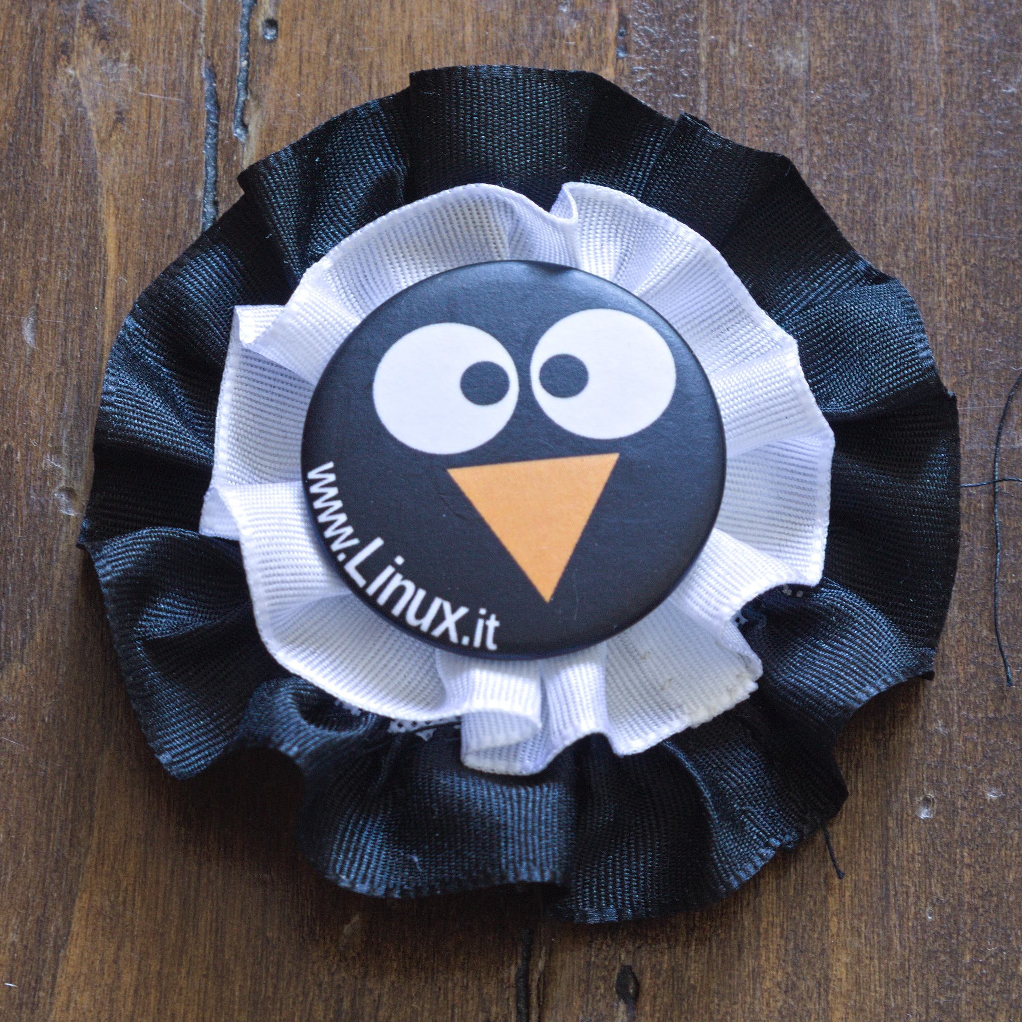 A cockade with just two gathered ribbons, starting with black
on the outside, then white, and a linux.it pin in the middle with
a black background and two eyes and an orange beak reminding of a
penguin.