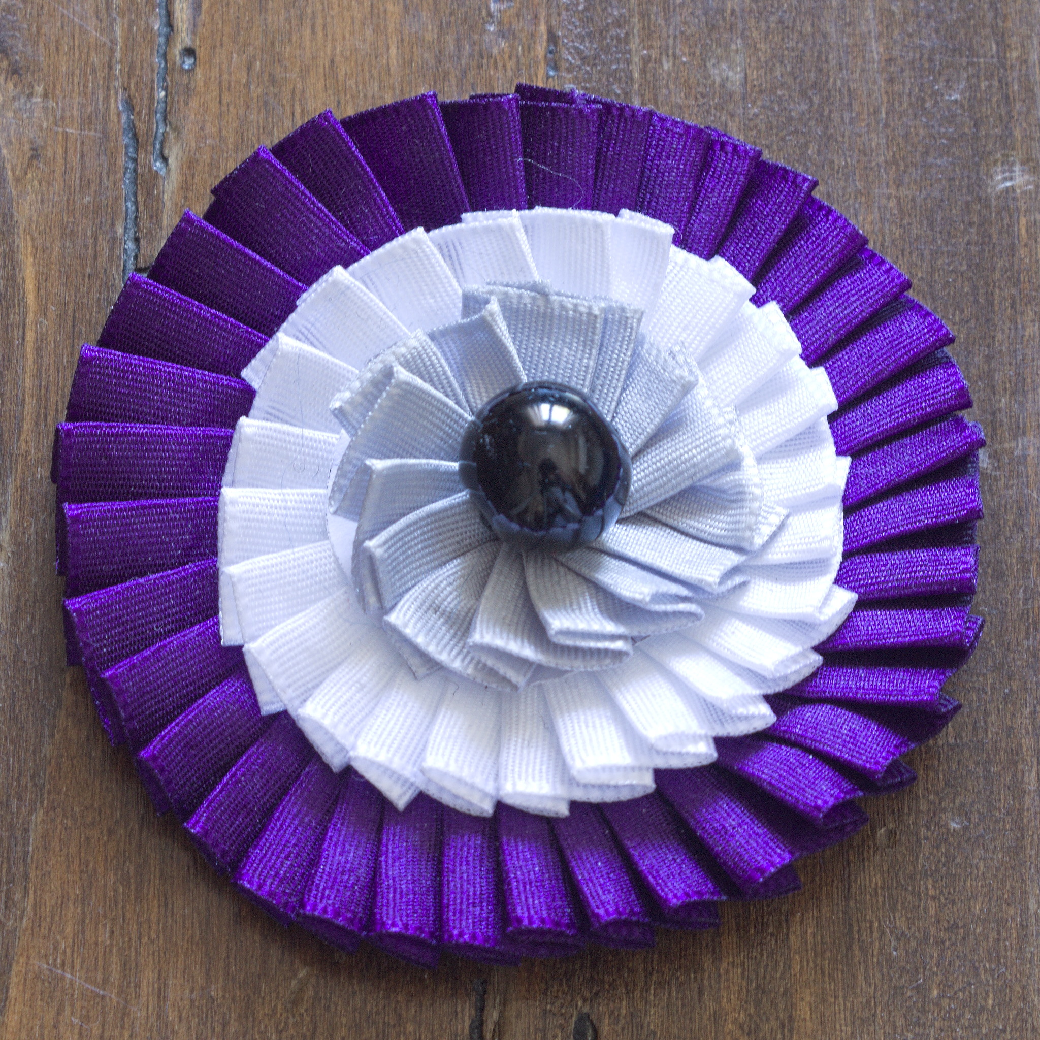 A cockade with tree ribbons, starting with purple on the
outside, then white, grey, and a black bead in the middle that is
a bit bigger than the one on the previous one. The pleating isn't
perfect, but neater than the previous one.
