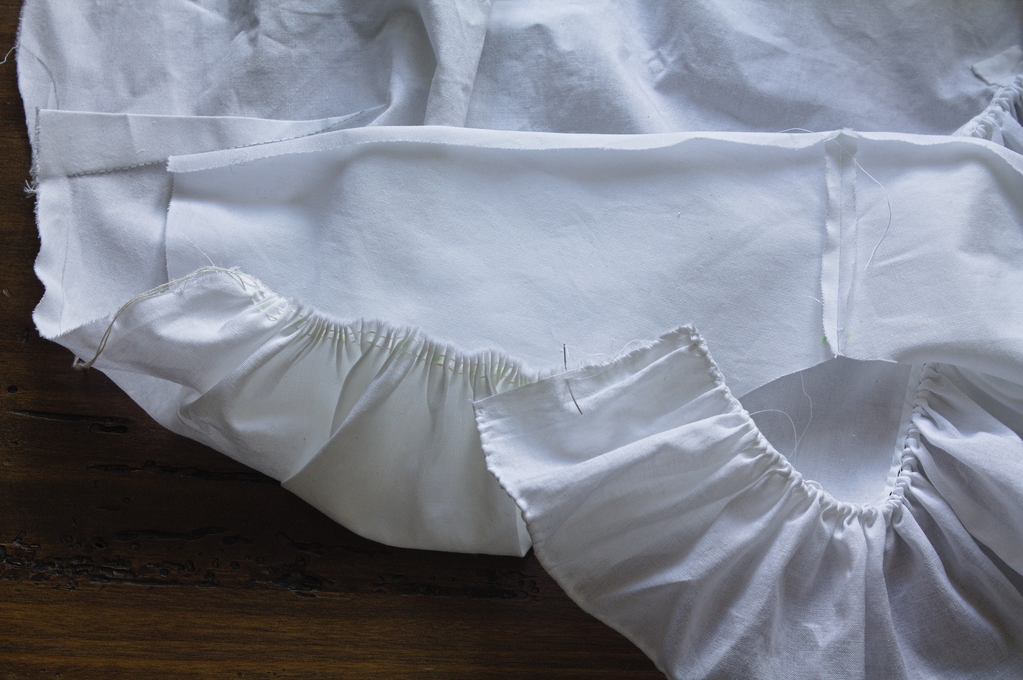 the top edge of a ruffle being whipstitched over some gathered
fabric; the rest of the unfinished shirt is visible in the
background.