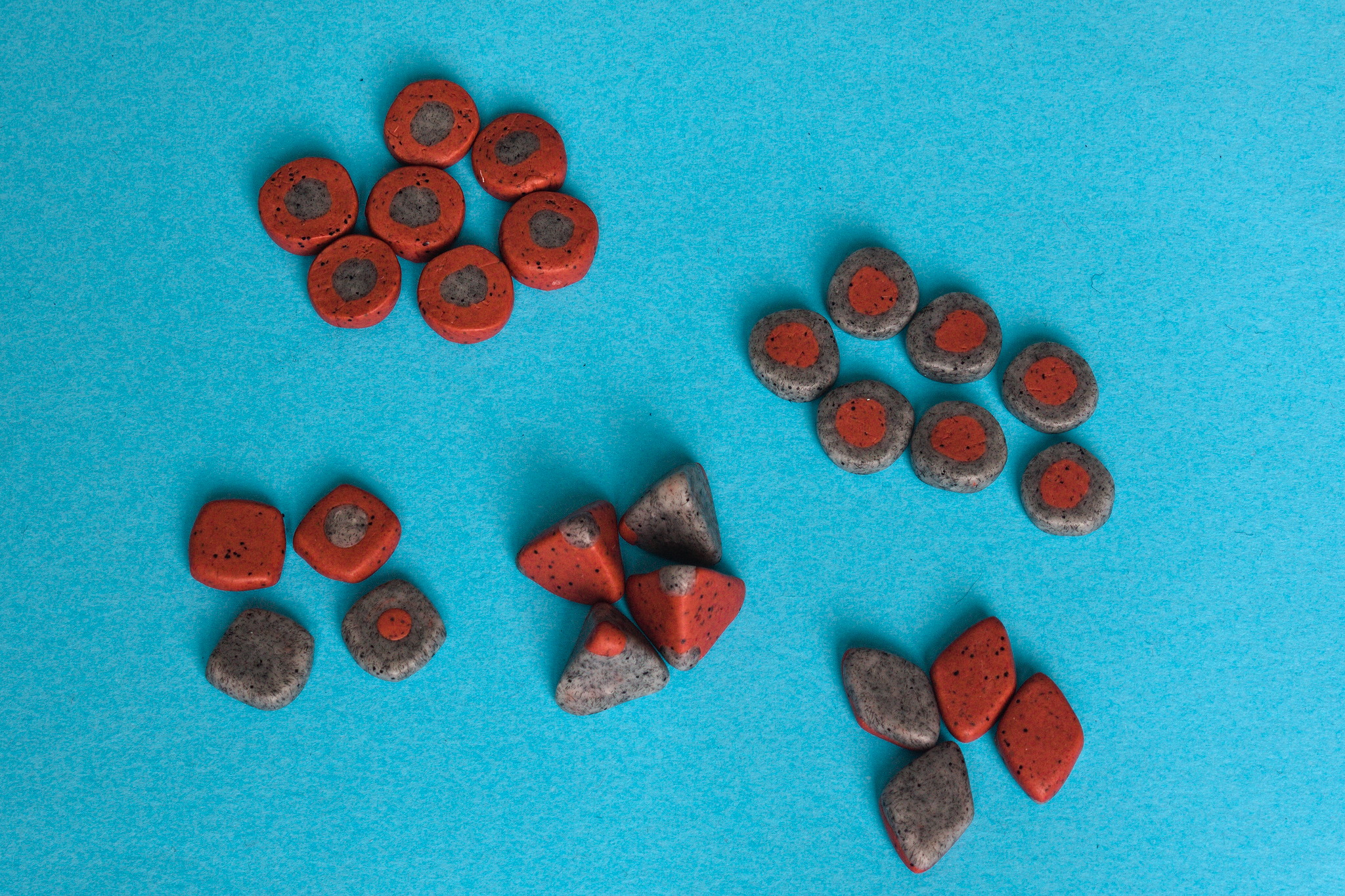 A set of red and grey tokens, tetrahedron dice, coins with one side marked with a dot that are square-ish rather than circular and four lozenge-shaped coins with each side of a different colour.