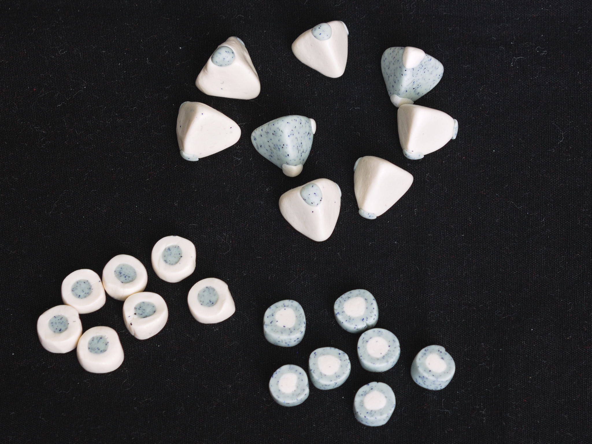 Royal game of Ur pieces in marbled grey and white plastic: the tokens are small coins in one colour with a small circle of the other colour in the middle, the dice are tetrahedrons in one colour with two points marked in the other colour.