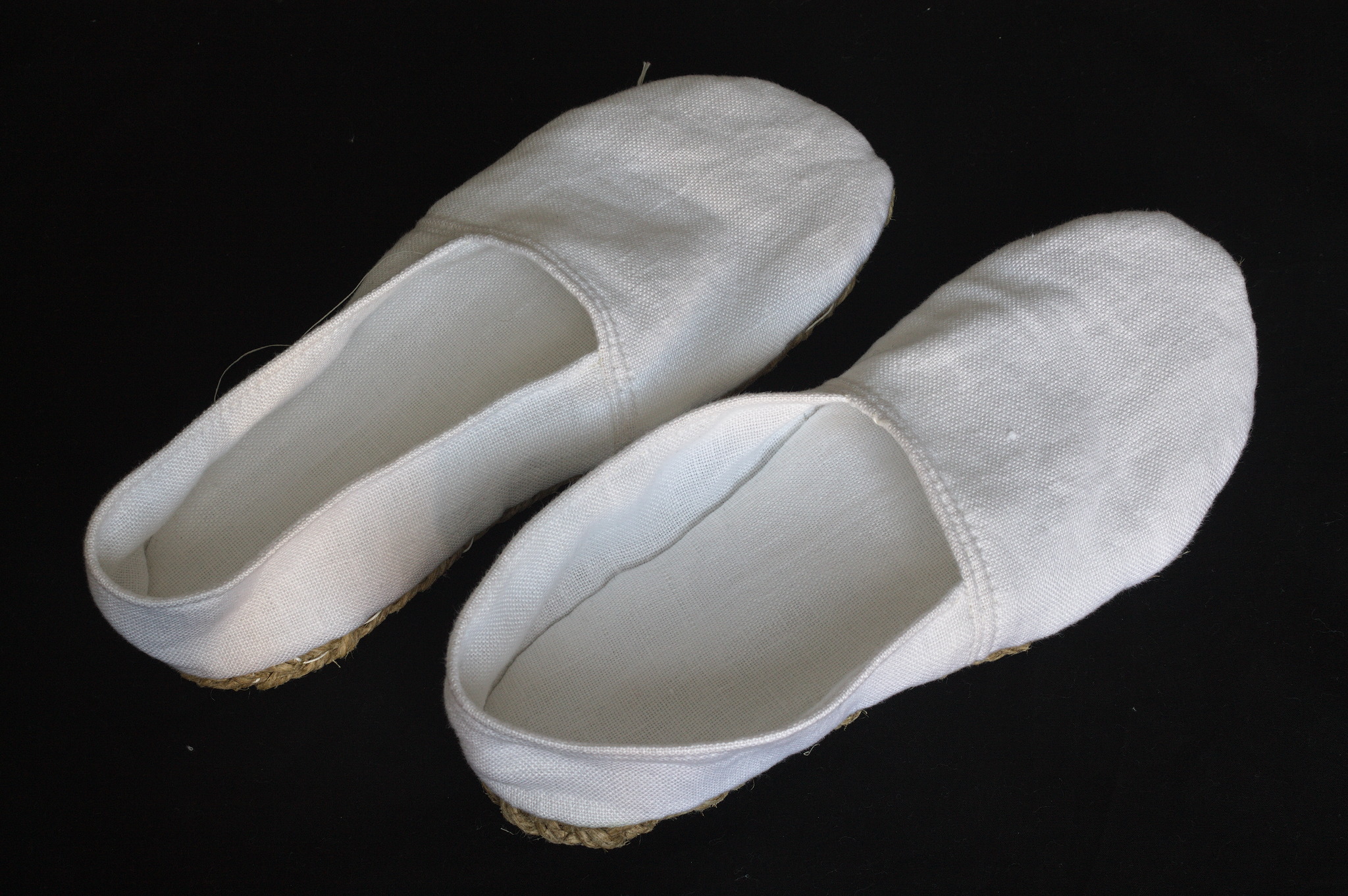 A pair of espadrille-like slippers in white fabric.