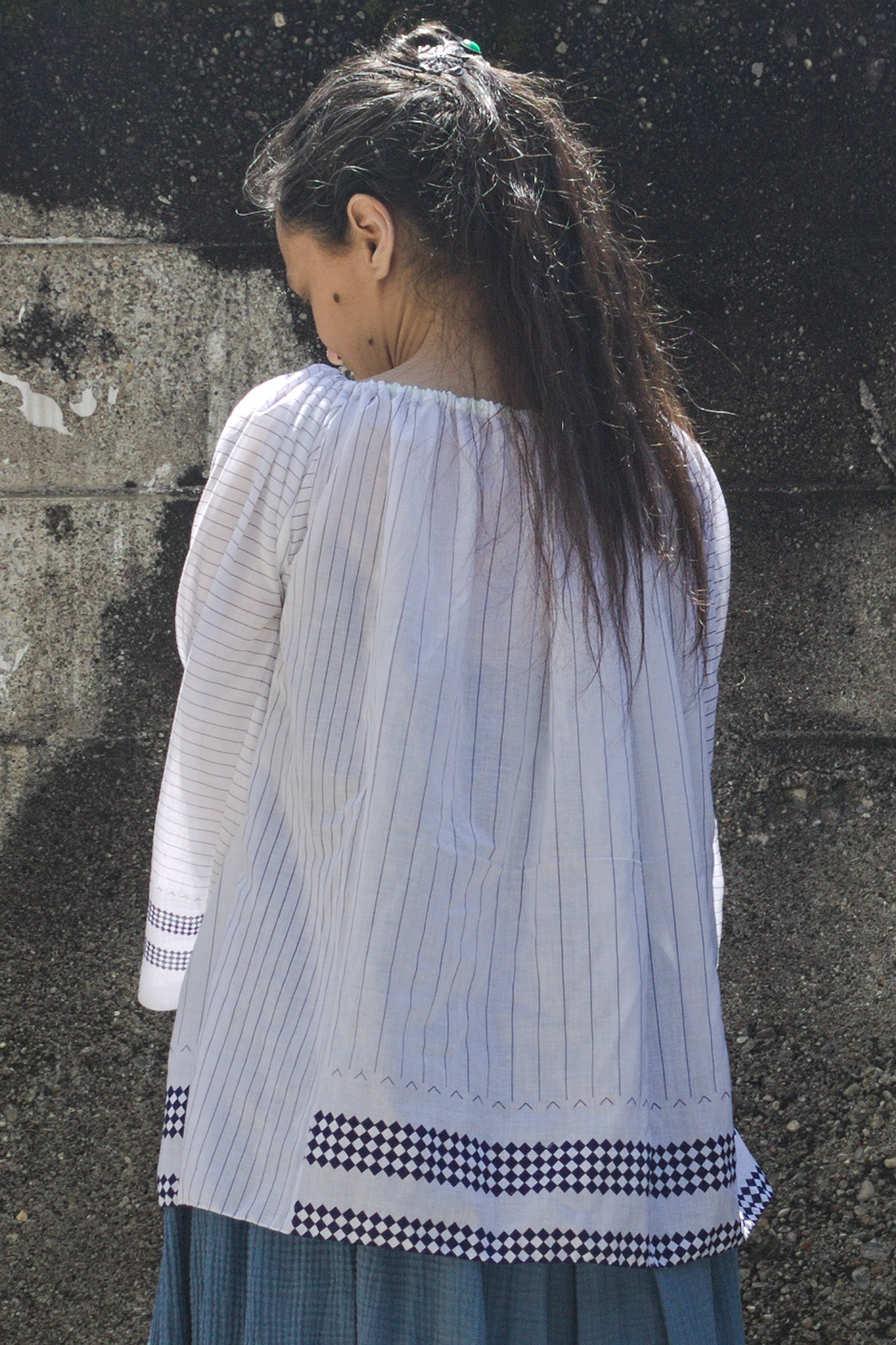 The worn top shown from the side back: there is a strip of vertical lines spaced closer together like on the sleeves, and it continues to the bottom rather than ending with a strip of lozenges.