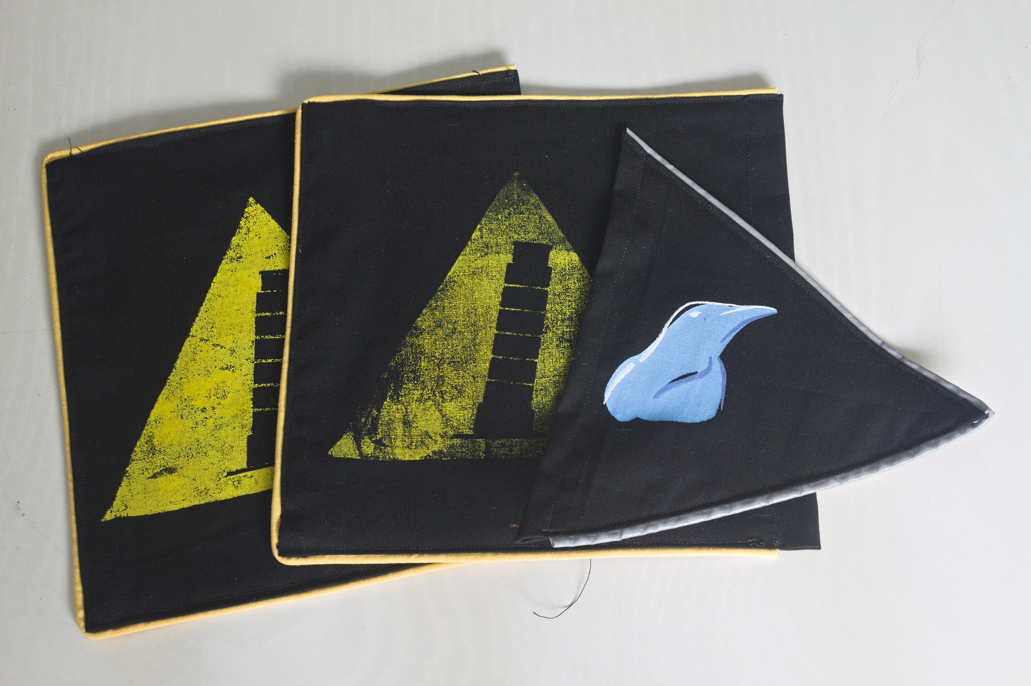 Three fabric banners: one is the one mentioned above, two are square with a yellow corded border, a yellow triangle and a tower of Pisa in black in the middle. The yellow triangles aren't perfectly flat yellow, but somewhat ruined, one more than the other.