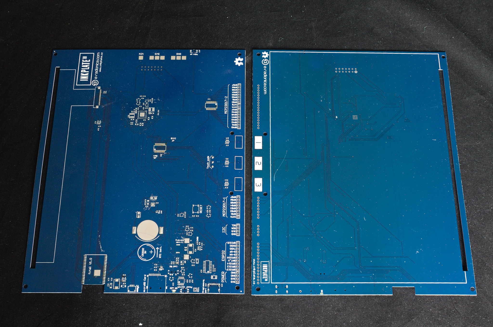 Two PCBs for the Inkplate 10 from eradionica, unpopulated. They are rectangles with a long slit close to one long side, a few holes and a notch at the bottom.