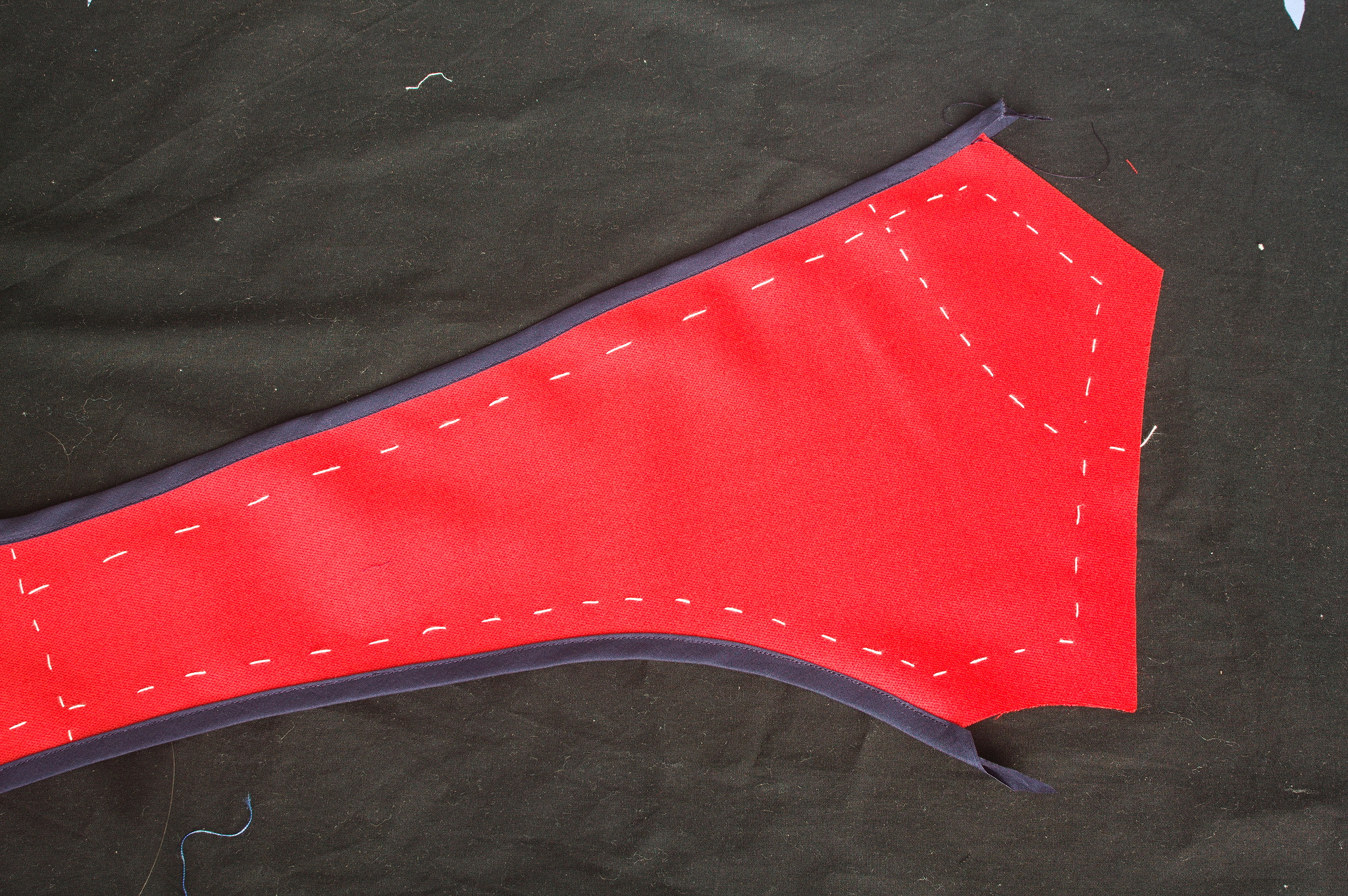 A shaped piece of red fabric with the long edges bound in navy
blue bias tape and all the seamlines marked with basting thread.