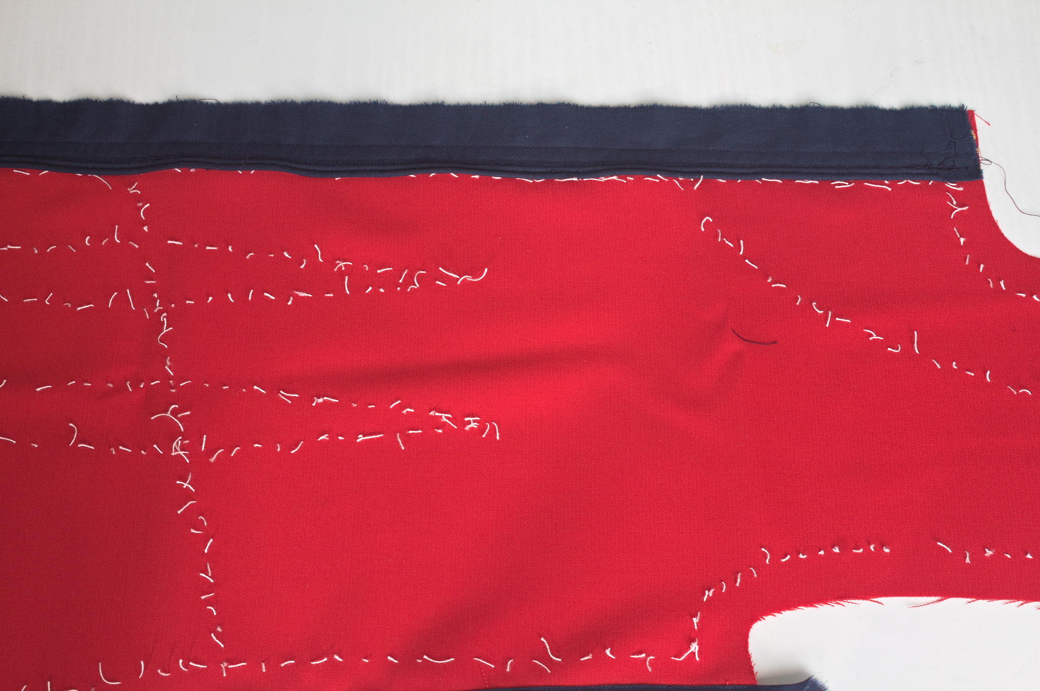 A bigger piece of fabric with tailor's tacks for the seams and
darts; at the top edge there is a strip of navy blue fabric sewn
to a wide seaming allowance, with two rows of cording closest to
the center front line.