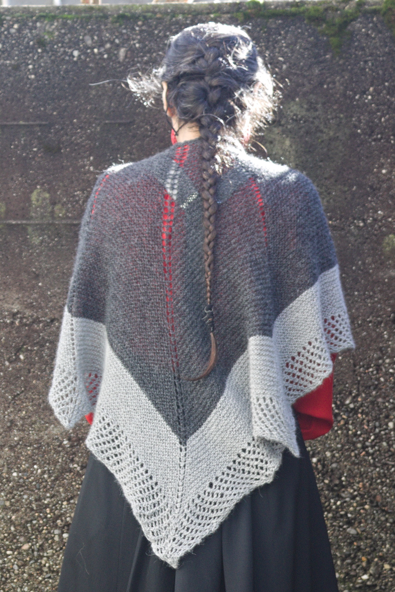 a woman wearing a shawl, seen from the back where it looks like
a big dark grey triangle with a light grey border and another
light grey border with a grid of holes. There is also a double
line of holes in the center of the back, and two single ones
towards the sides.