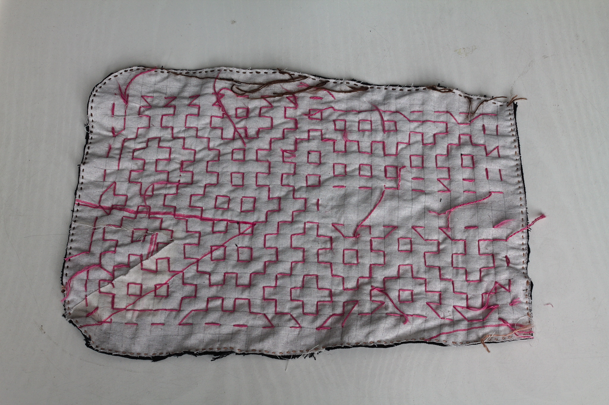 The wrong side of a pocket piece, showing a light coloured fabric
with a grid drawn in pencil, a line of small stitches all around
the edges and a mess of thread ends left hanging.