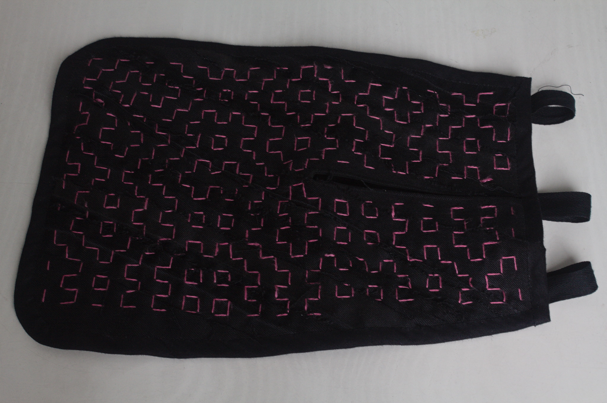 A 18th century pocket in black jeans with a random pattern of pink running stitches forming squares and other shapes. The unfinished edges of the pieces of jeans can be seen, running more or less diagonally.