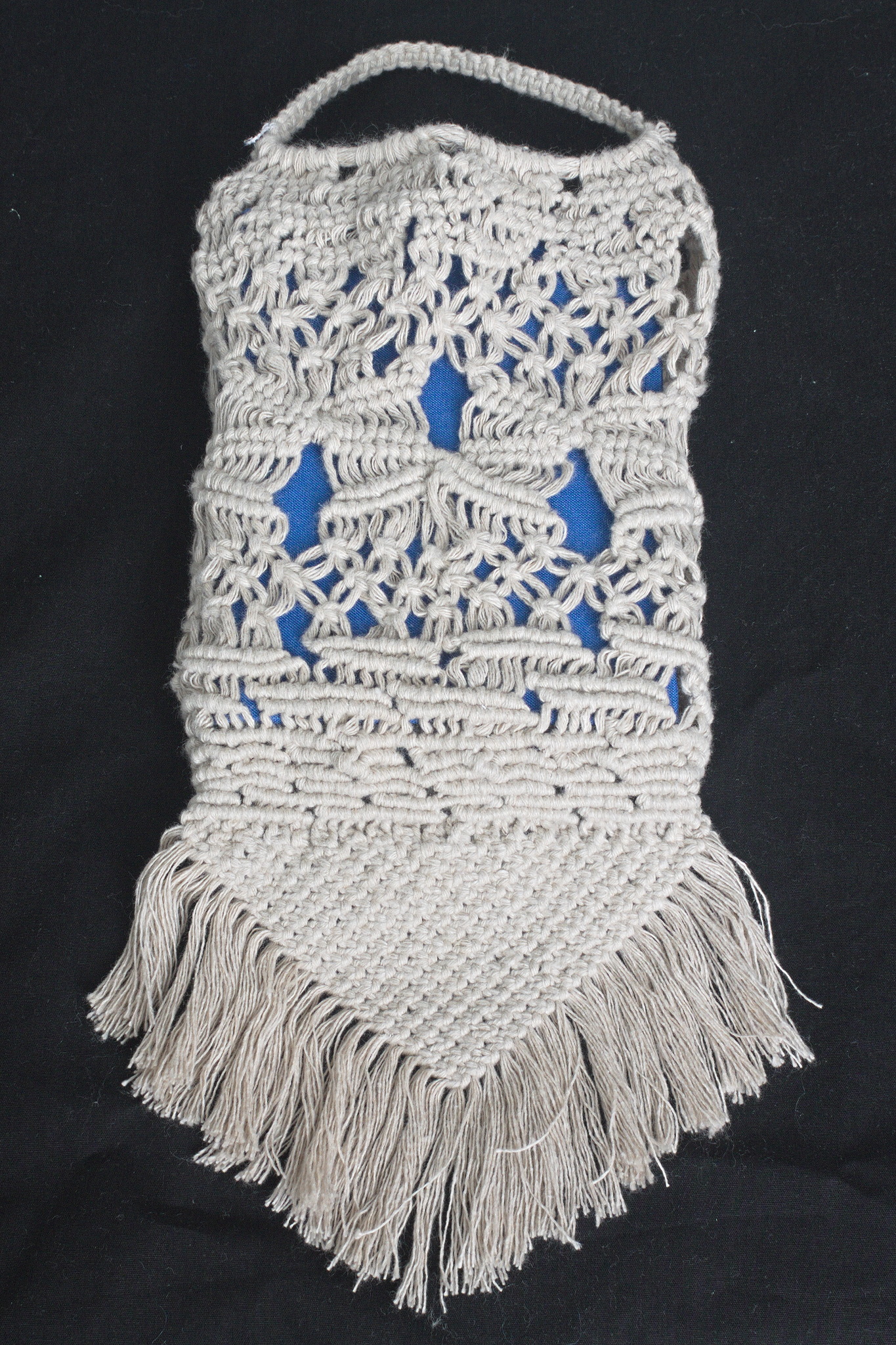 a macrame bag in ~3 mm ecru yarn, with very irregular knots of
different types, holding a book with a blue cover. The bottom part
has a rigid single layer triangle and a fringe.