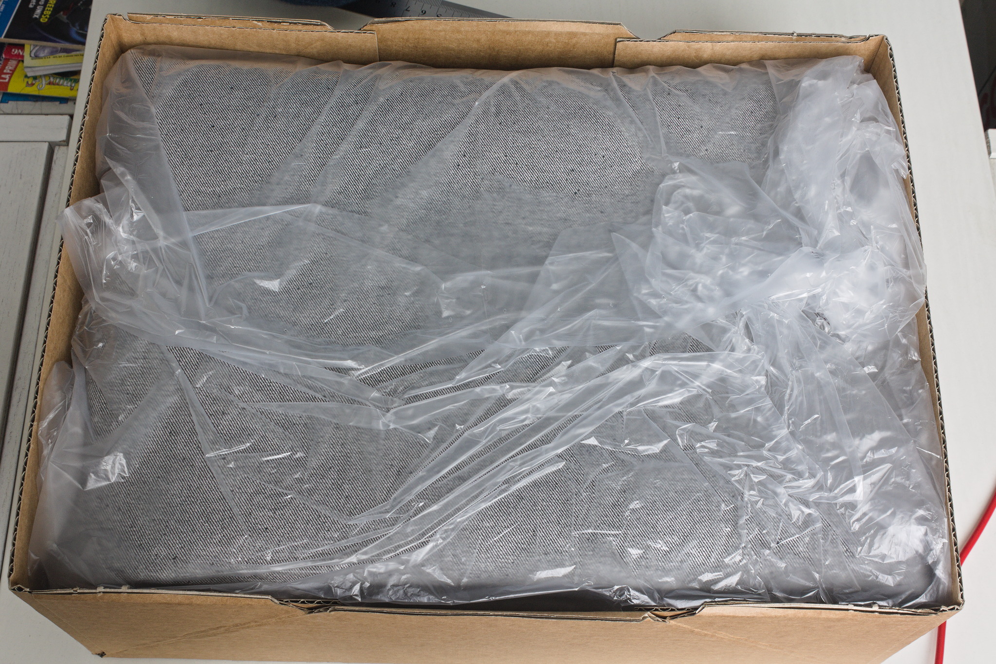 a cardboard box with neatly folded black denim, covered in semi-transparent plastic.