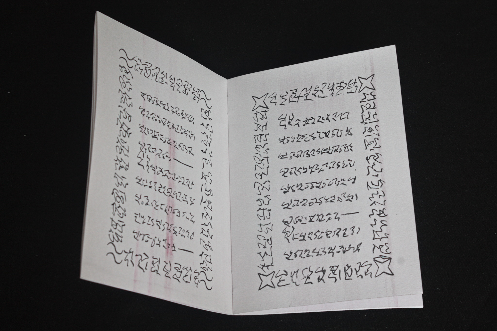 An open booklet with lines that look like some kind of cursive
non-alphabetic script, framed by a border in the same script and
four symbols in the corners.