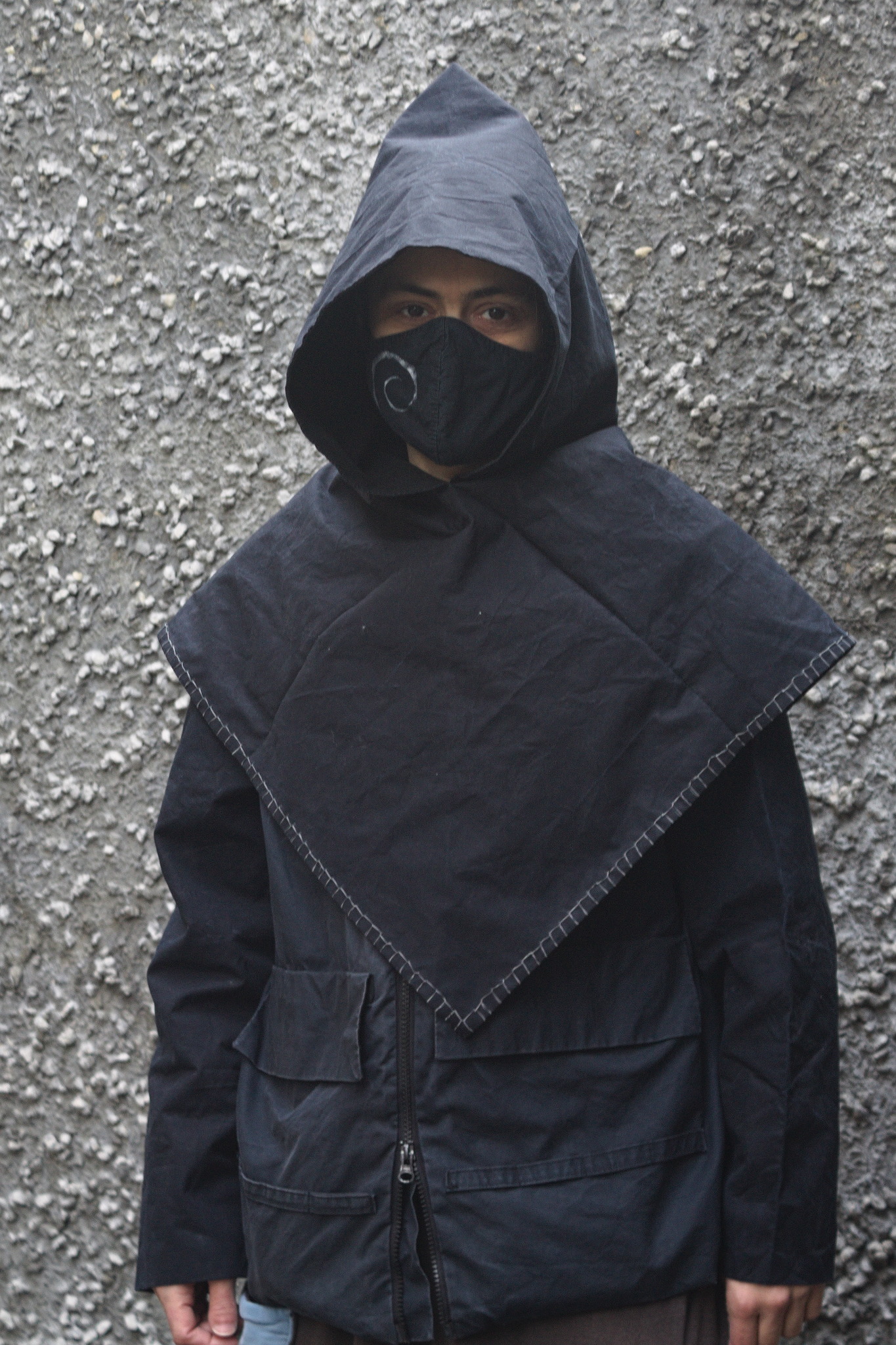 a person wearing a relatively boxy water resistant jacket with
pockets and a zipper, and a detached hood with a big square cowl
that reaches mid-torso.