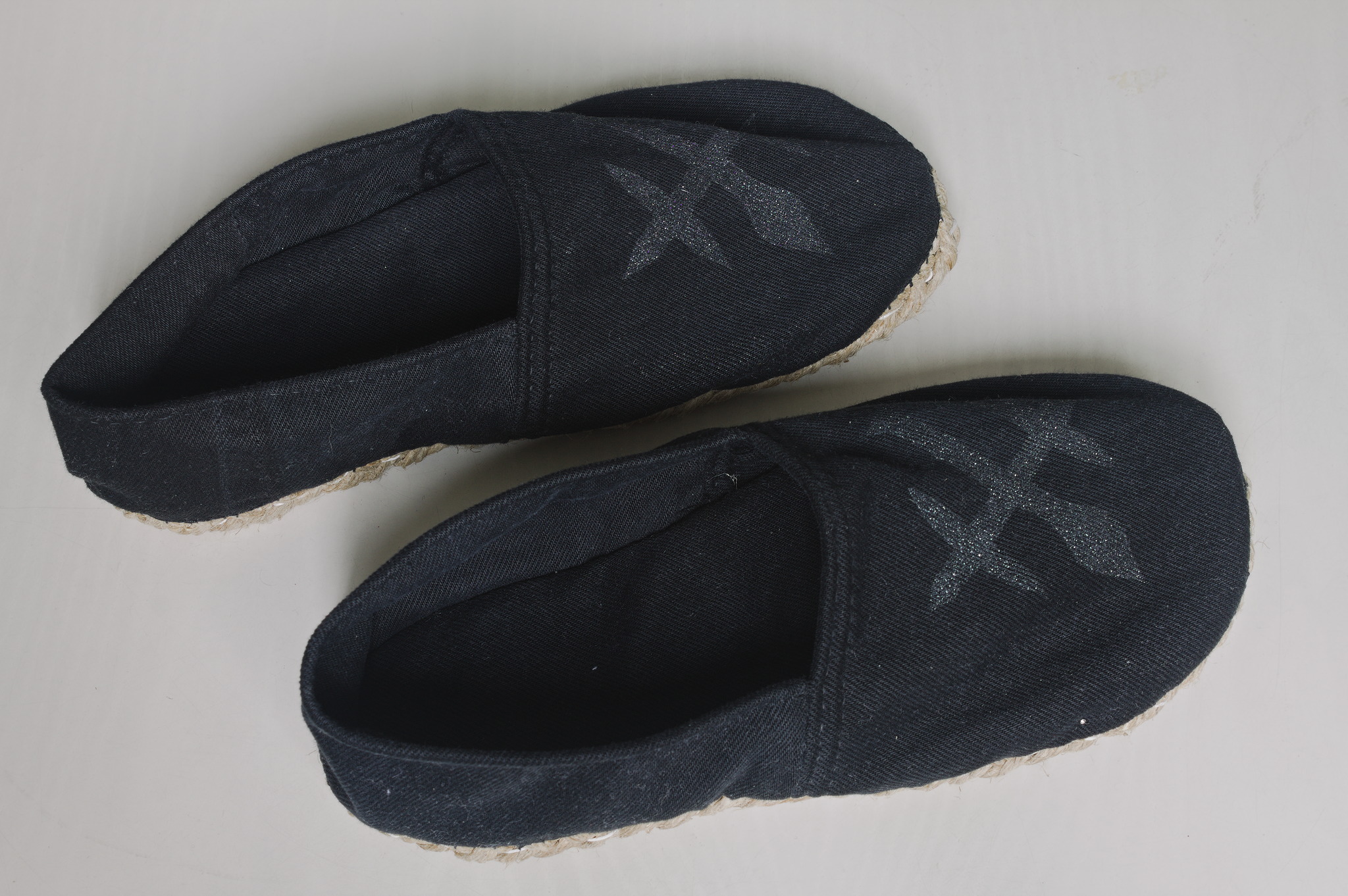 A pair of espadrille-style slippers in black denim with a shiny
black design on the uppers and twine soles.