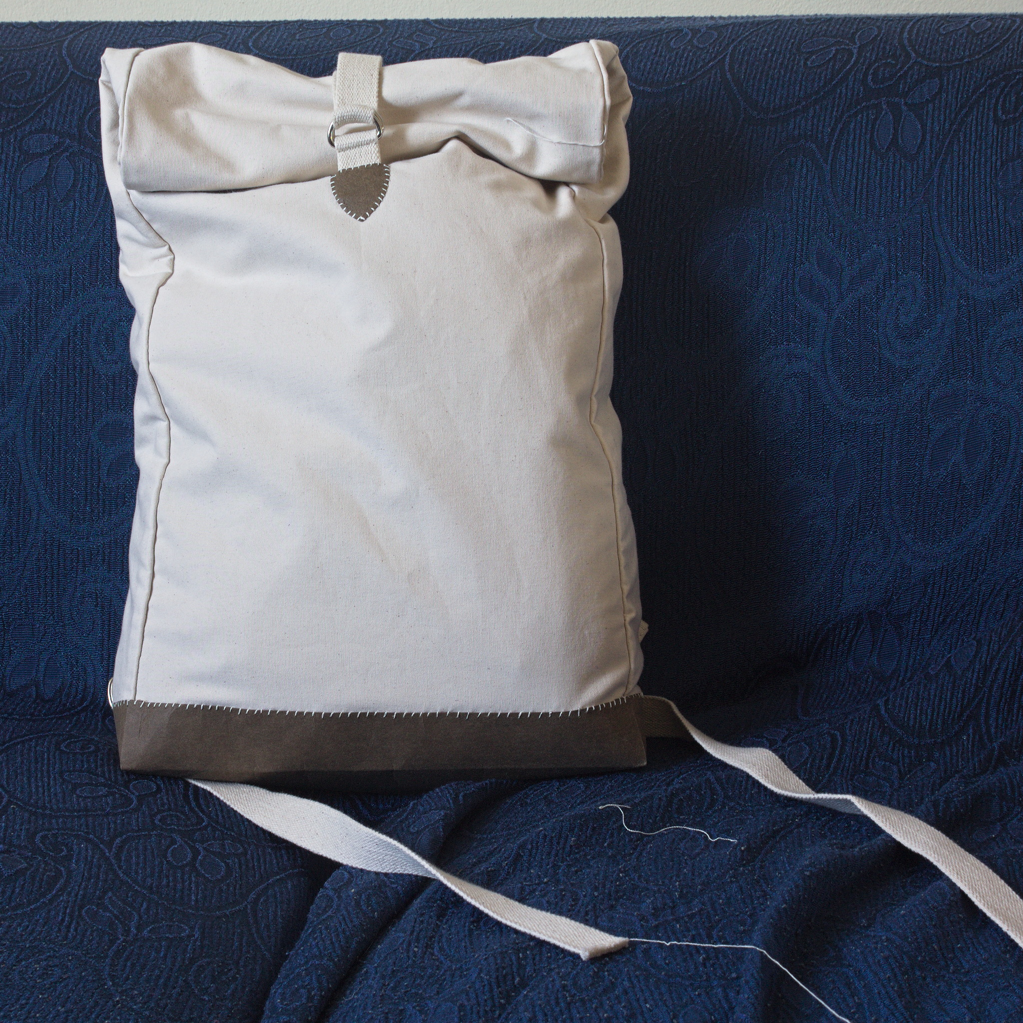 a backpack in a cream fabric with a short dark brown bottom; it
closes by rolling down the top and is kept closed by a strap that
feeds through two D-rings.