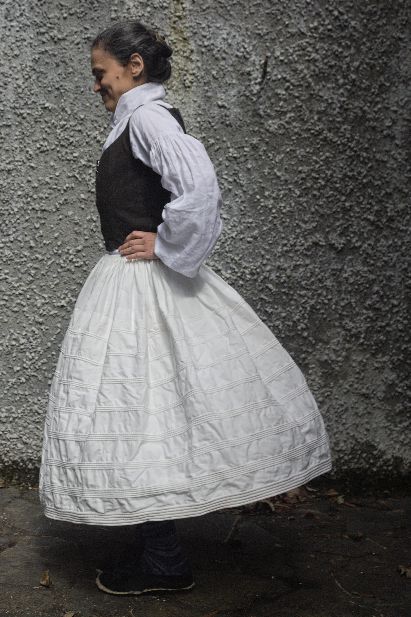 A woman turning fast enough that her petticoat extends a
considerable distance from the body. The petticoat is white with a
pattern of cording from the hem to just below hip level, with a
decreasing number of rows of cording going up.