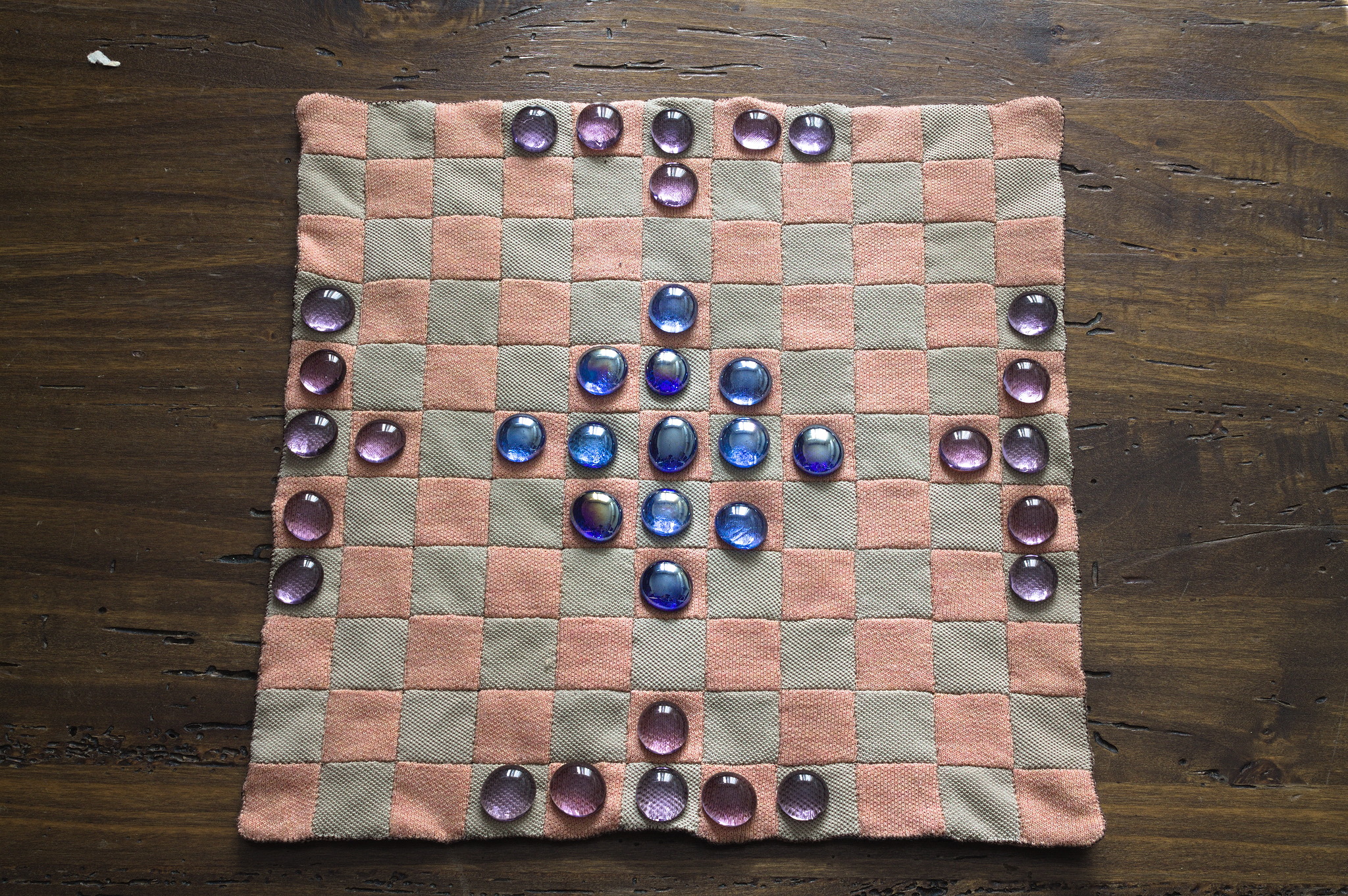 The squares sides of the mat, with some blue and purple stones 
in the starting position for a hnefatafl game.