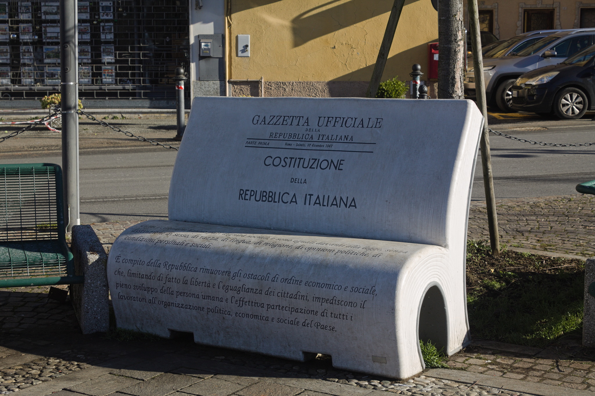 A bench in the shape of an open book, half of the pages folded in a reversed U to make the seat and half of the pages standing straight to form the backrest. It has the title page and beginning of the Constitution of the Italian Republic.