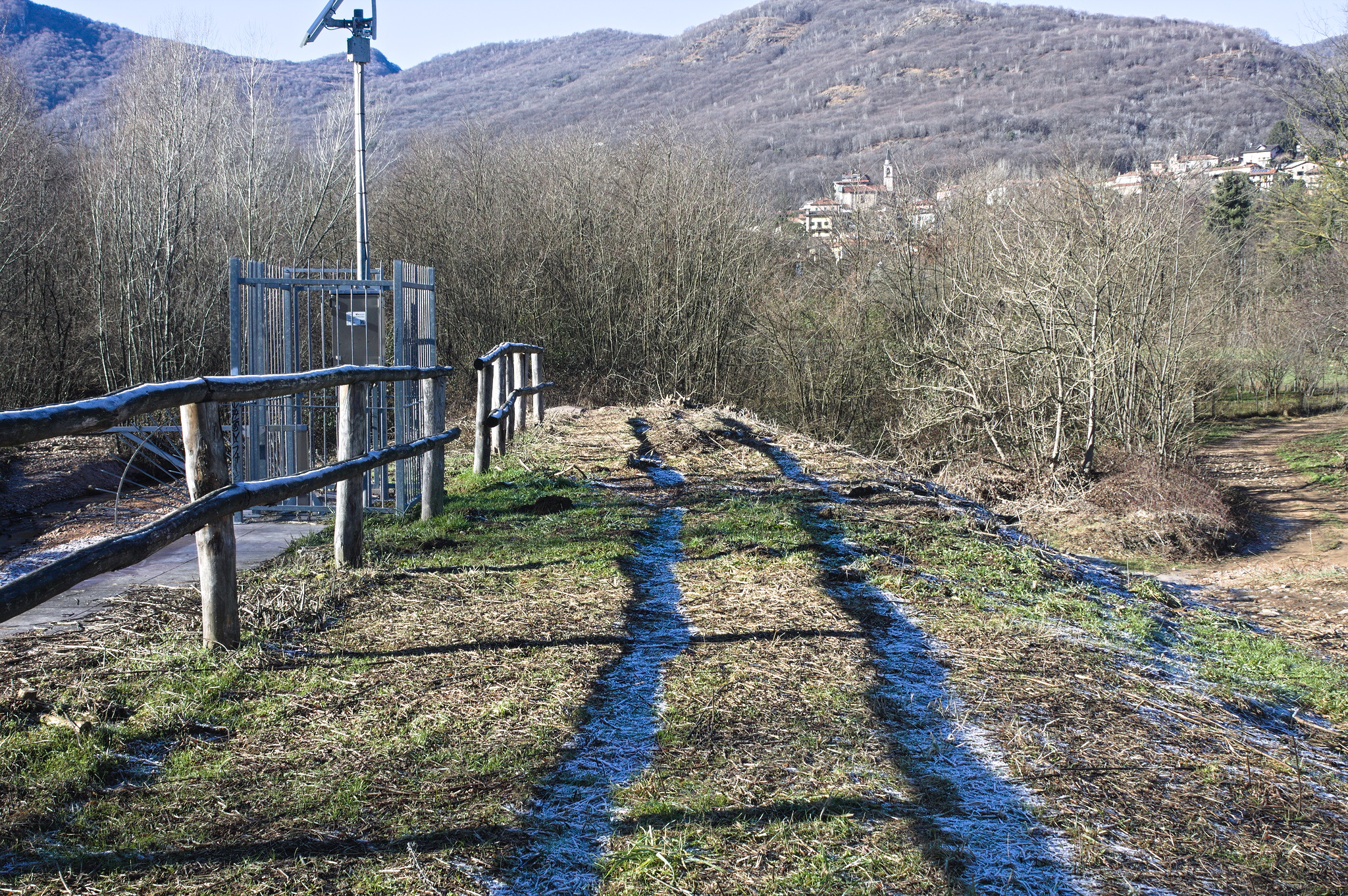 Dried winter grass with two strips of frost, exactly under the shade of a fence.