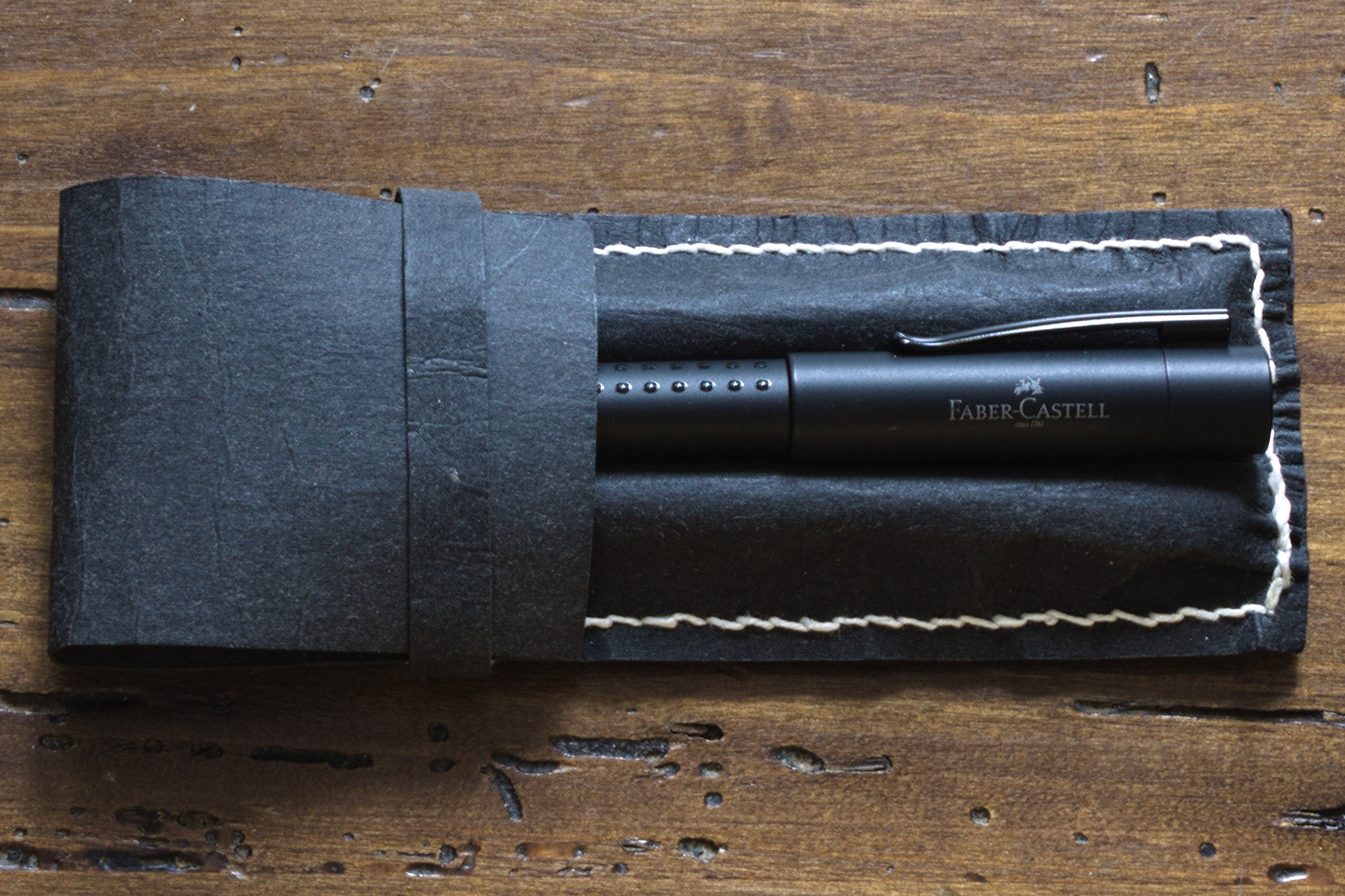 a case similar to the one above, but this one only has two slots, and there is a a Faber Castell pen nested on top of the case between the two slots. Here the stitches are white, and in a coarser thread.