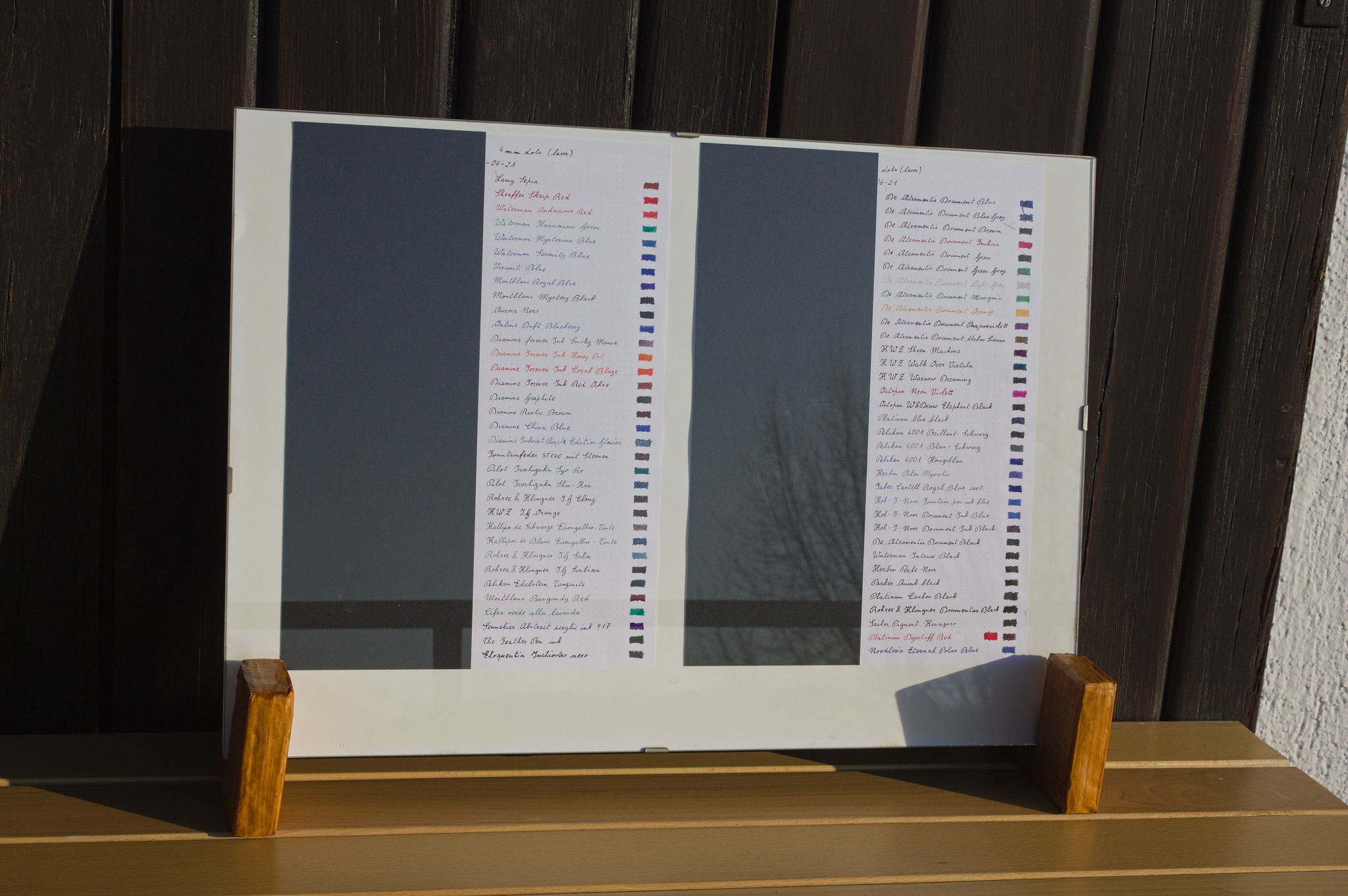 A borderless frame set on a table outdoors, with two sheets of
paper a vertical half of which is covered by black paper, while
the other half has lines with an ink name and a small filled
rectangle, all in the ink itself.