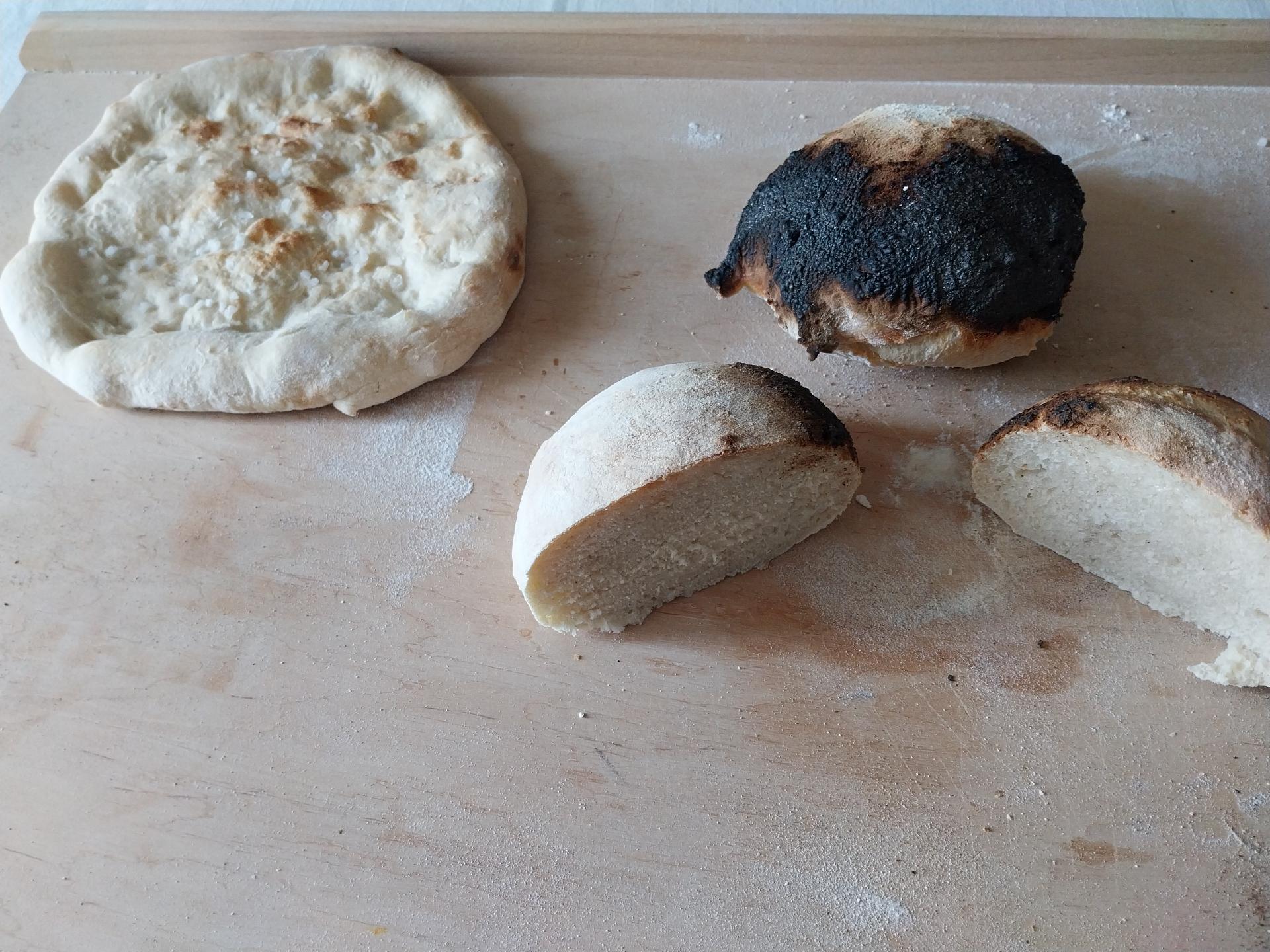 Another flatbread with coarse salt and two bread rolls, one of which is completely carbonized on one side. The other one has been cut, and while it has a carbonized spot, it is also well cooked in the middle, and perfectly edible.