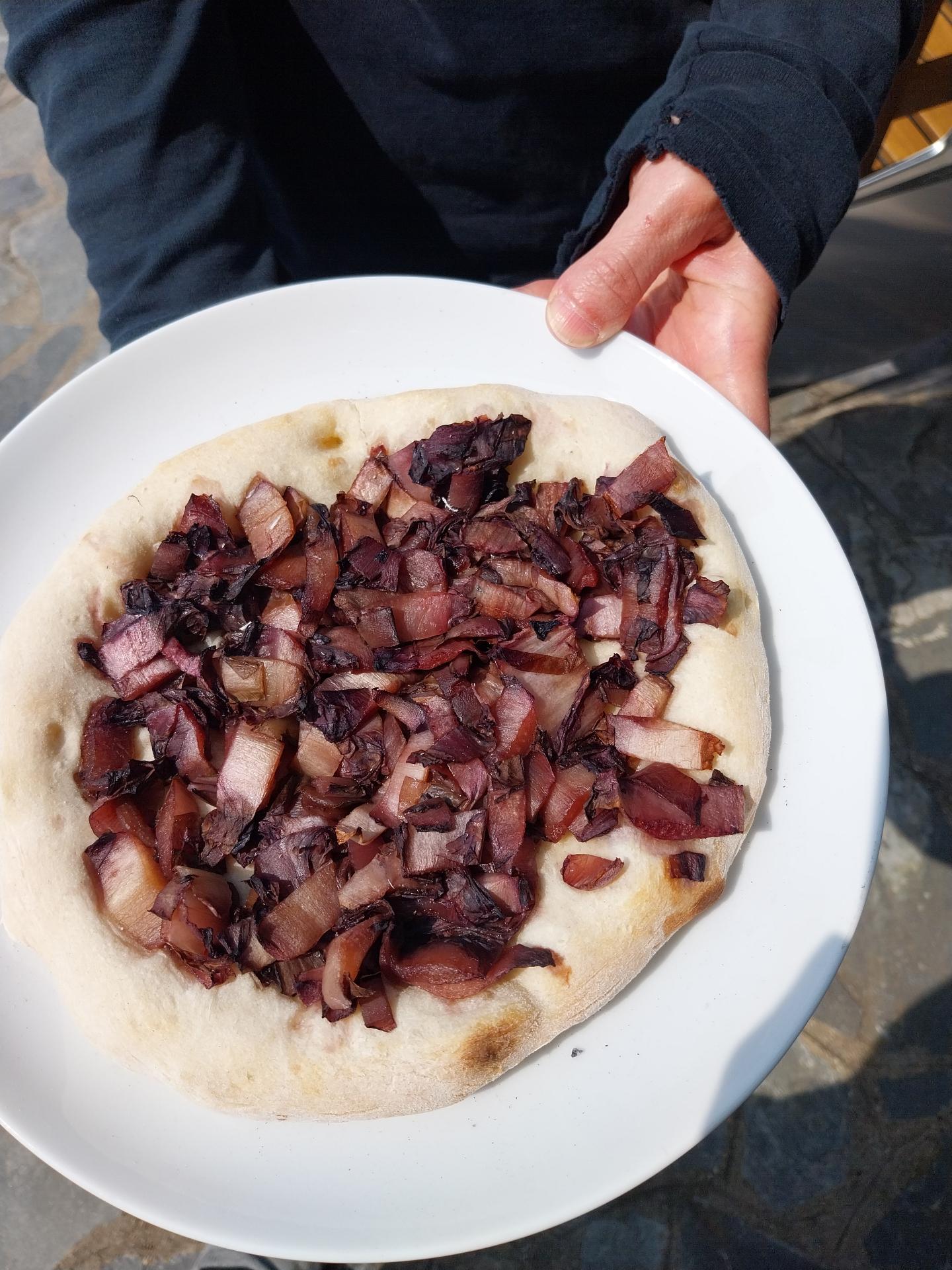 Another flatbread on the same plate, this time it's about 4 cm smaller than the plate on all sides, and it's covered with brownish-red chopped up vegetables.