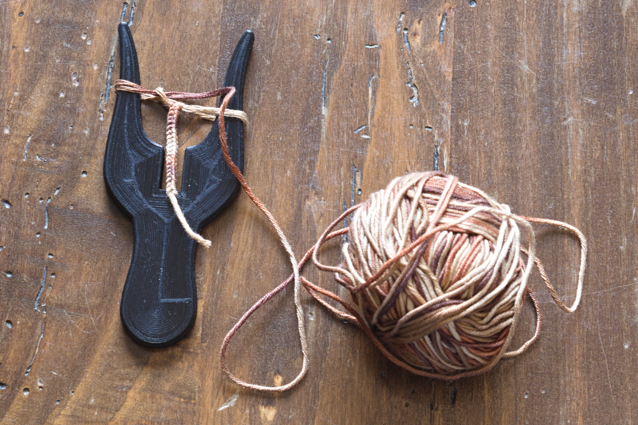 A lucet fork: a two pronged device with a handle with yarn
wrapped once around each fork and a knot forming in the middle,
out of which a piece of cord is growing. The working yarn is in a
ball nearby.
