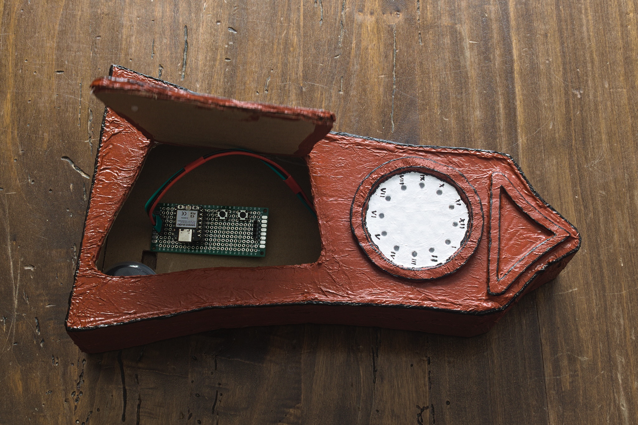 the clock turned 90°, with the door open showing the board
inside, plus a hint of a round plastic container that housed the
microcontroller board. A rectangular hole about the size of an USB
cable is visible in the back of the clock.