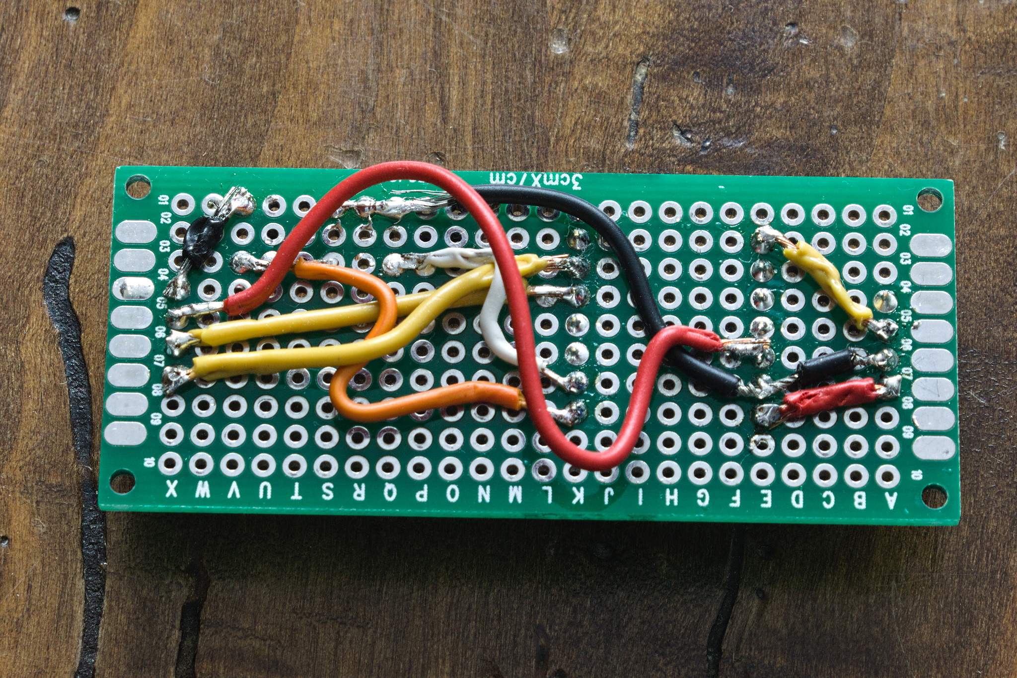 A rat nest of mostly colour-coded wire that cross each other.
badly soldered to the back of a bit of perfboard, with heat damage
on the wire insulation.